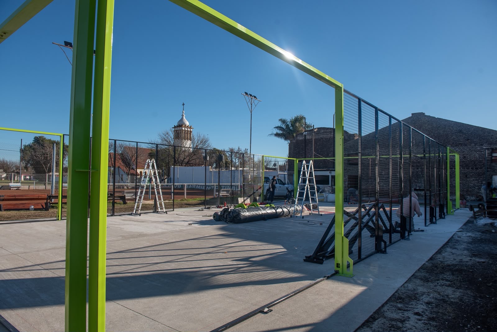 Estructura de la cancha de pádel del Club Sarmiento con la iglesia de Timbúes de fondo